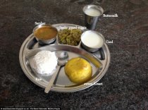 South Indian school children eat off a thali plate which has white rice, sambar (dhal), smoked gourd vegetable stir-fry, curd, buttermilk and kesari, a type of sweet dessert made from semolina